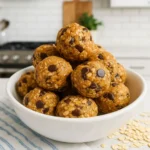 No Bake Energy Bites stacked in a white bowl with oats and chocolate chips